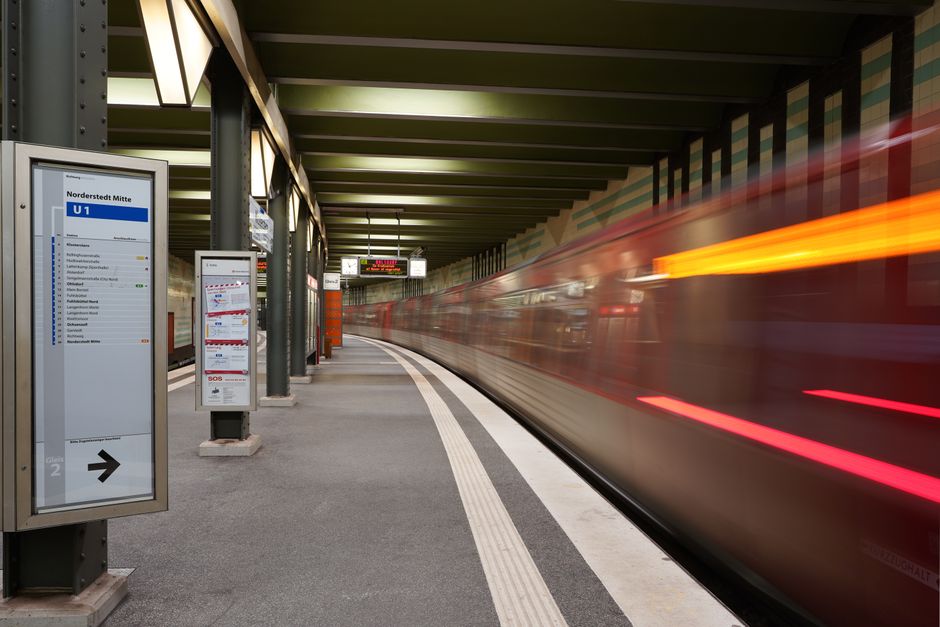 A blurred motion image of a yellow tram moving rapidly along a sleek, modern city street. The tram appears to be in an indoor or underground station with reflective, dark tiled walls featuring geometr